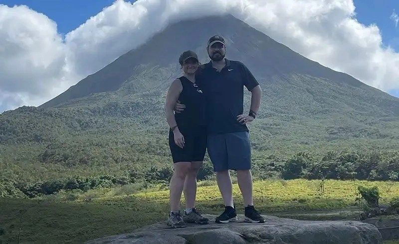a man and woman standing on a rock with a mountain in the background