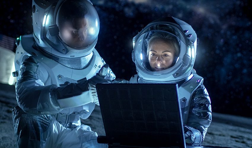 Two Astronauts Wearing Space Suits Work on a Laptop