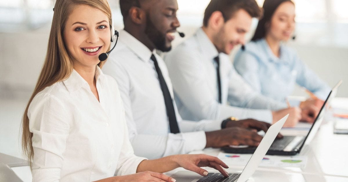 Attractive business people in suits and headsets are smiling while working with laptops in office