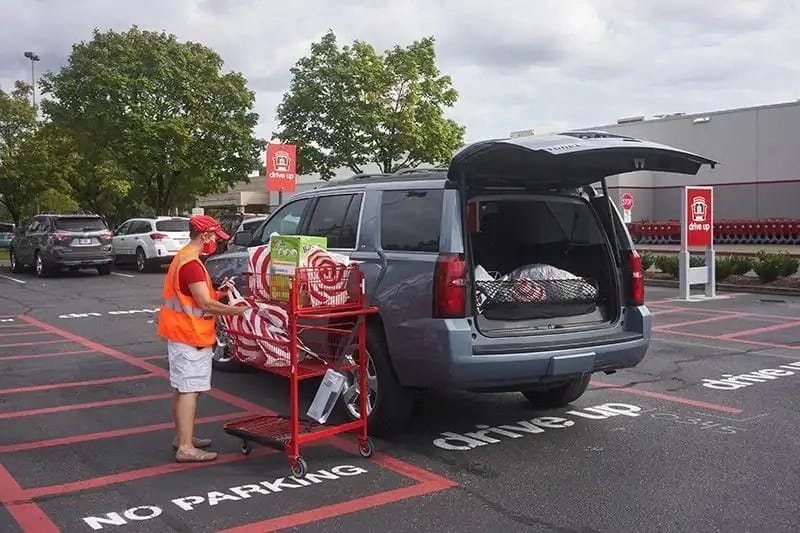 store employee brings bagged items out to a customers parked car during a pandemic - open in a new tab