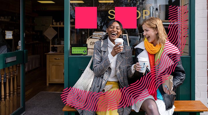 Two happy women laughing together outside a coffee shop